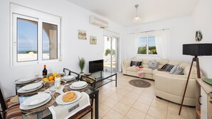 A modern living room with a sofa, a dining table set for two, and a TV. - Villa Maia - Three Bedroom Villa, Sleeps 6 (Rhodes)