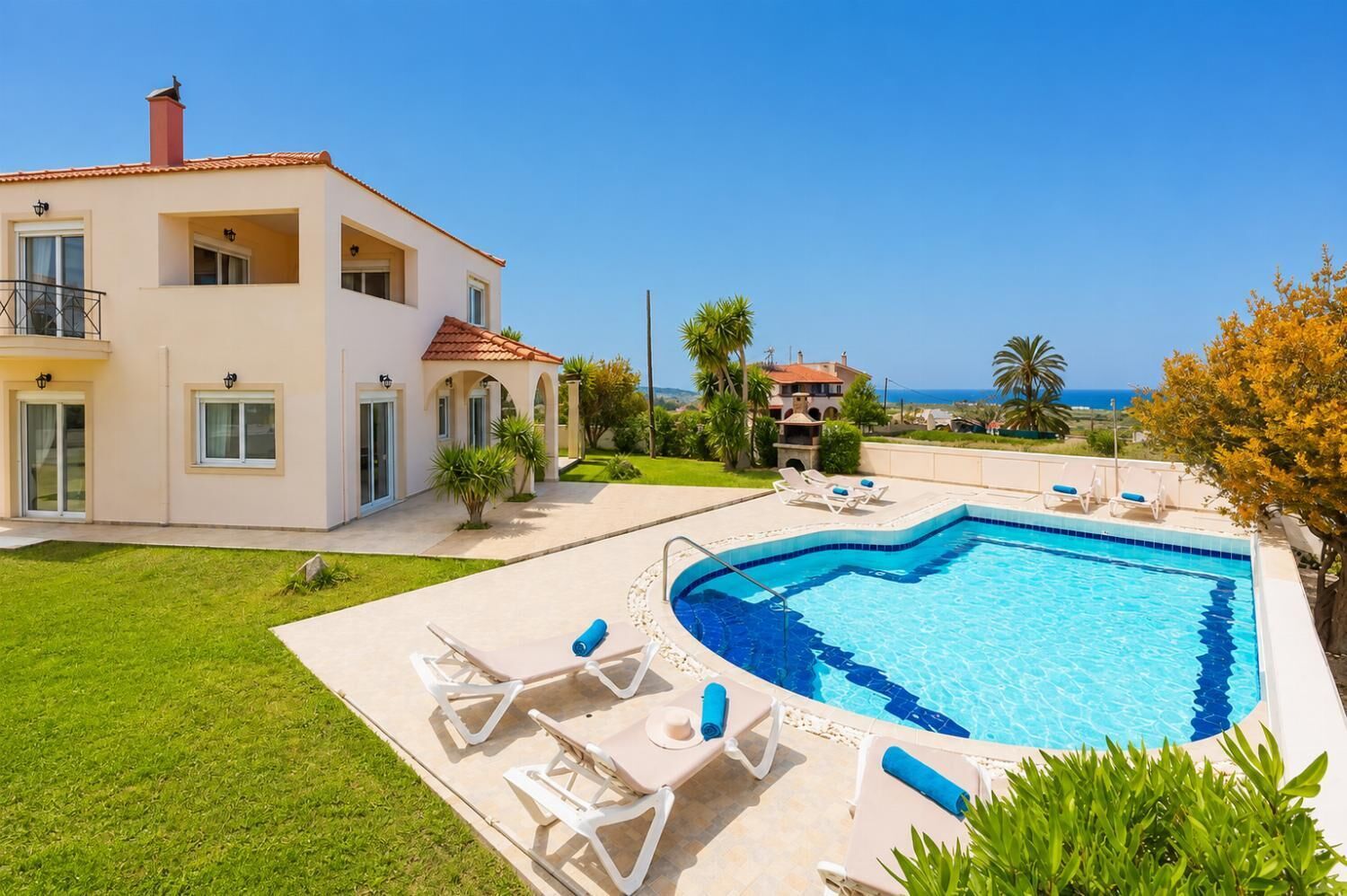 Una casa de dos pisos con piscina, mobiliario exterior y vista al mar.
