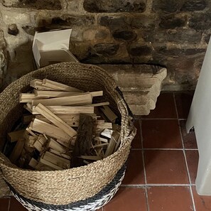 A woven basket filled with firewood next to a stone wall and a tiled floor. - Beautiful Haven Retreat in Sandwich (Sandwich)