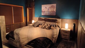 Ein Schlafzimmer mit einem Bett, Nachttischen, einem Gemälde und einem Fenster mit Jalousien.