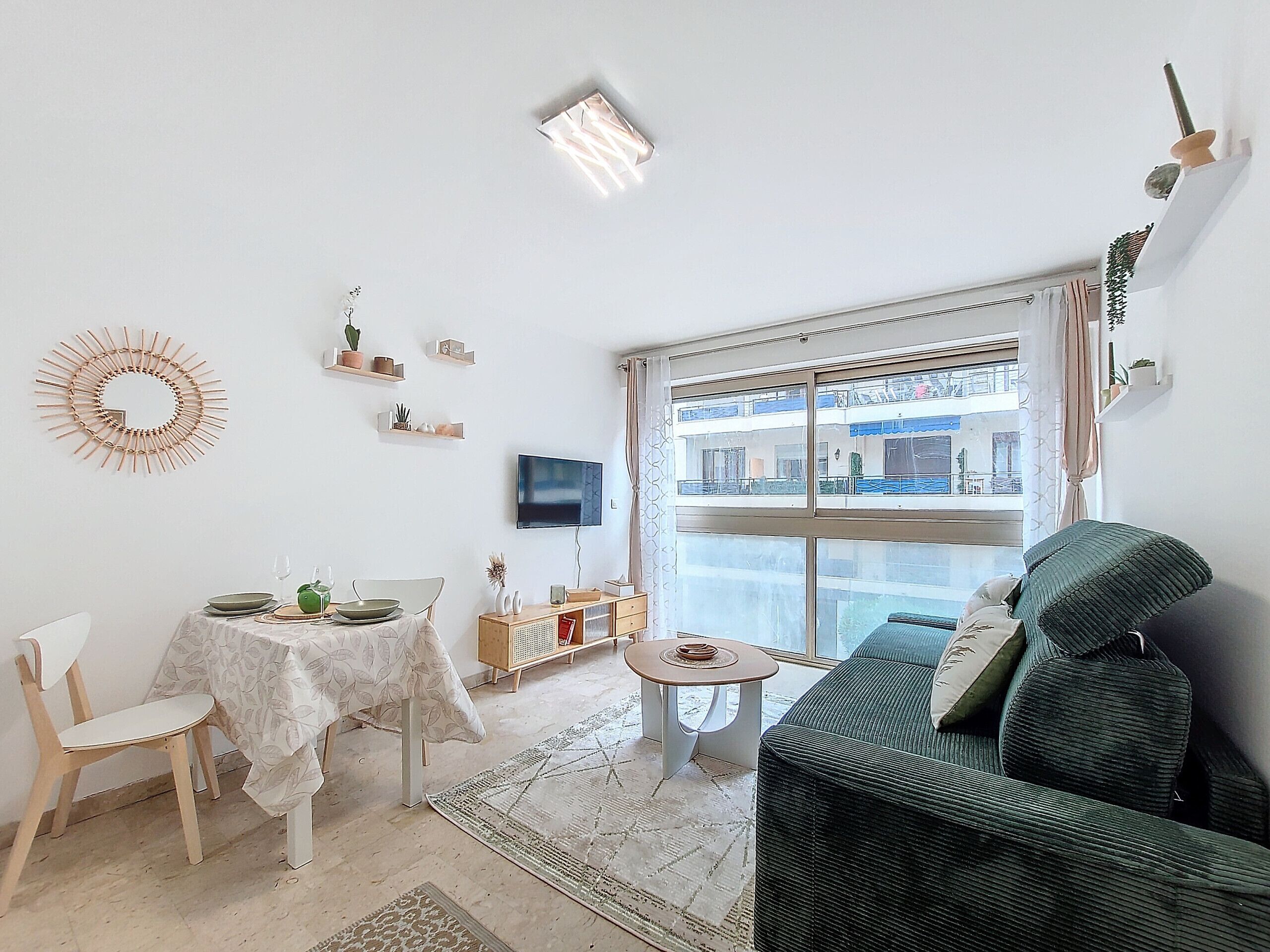 Ein Wohnzimmer mit einer Couch, einem Esstisch mit Stühlen, einem an der Wand befestigten Fernseher und einem großen Fenster mit Blick auf Gebäude.