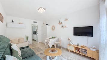 Ein modernes Wohnzimmer mit einer Couch, einem Esstisch, einem Fernseher und einer Küche im Hintergrund.