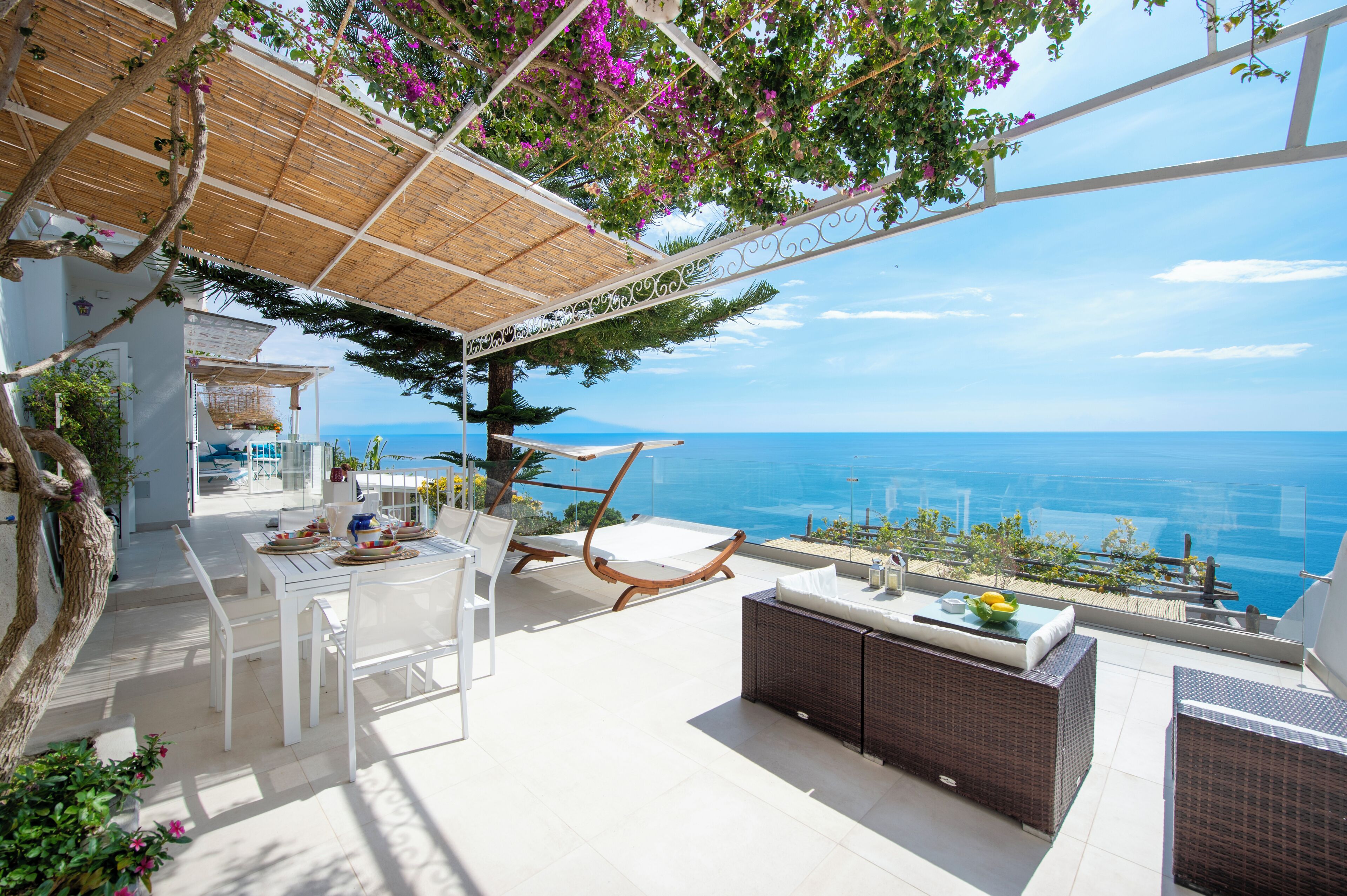 A terrace with a dining table, chairs, a sofa, and a wicker sofa with cushions.