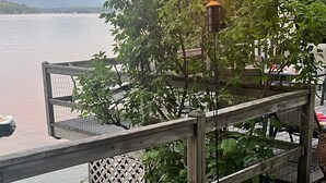 A waterfront patio with a wooden railing, potted plants, and a table with chairs. - Winnipesaukee Heirloom Cottage (Meredith)