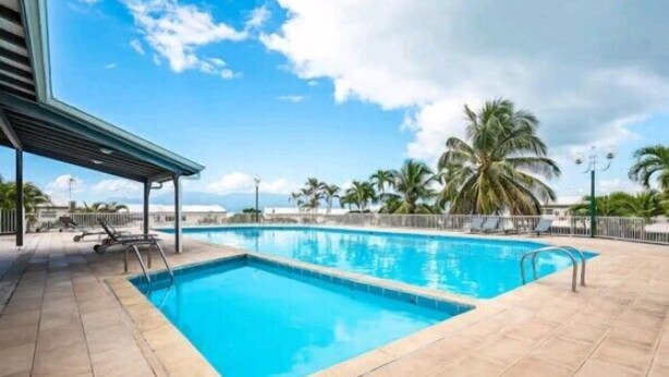 A rectangular swimming pool with clear blue water, surrounded by a tiled deck with lounge chairs.