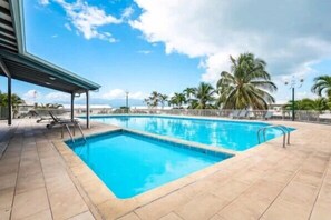 A rectangular swimming pool with clear blue water, surrounded by a tiled deck with lounge chairs.