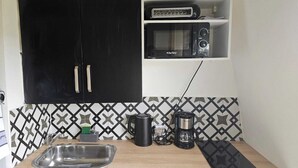 A compact kitchen with a black cabinet, a microwave, a coffee maker, and a sink.