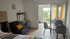 A hotel room with a bed, a desk, a chair, and a balcony with yellow curtains.