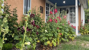 Ett hus med en inglasad veranda, siffran ’3’ på dörren och olika blommande växter i trädgården.