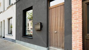 A modern building with a large wooden door, a small window, and a security box on the wall. - Charming Ostend Home: Near Beach & City Center (Oostende)