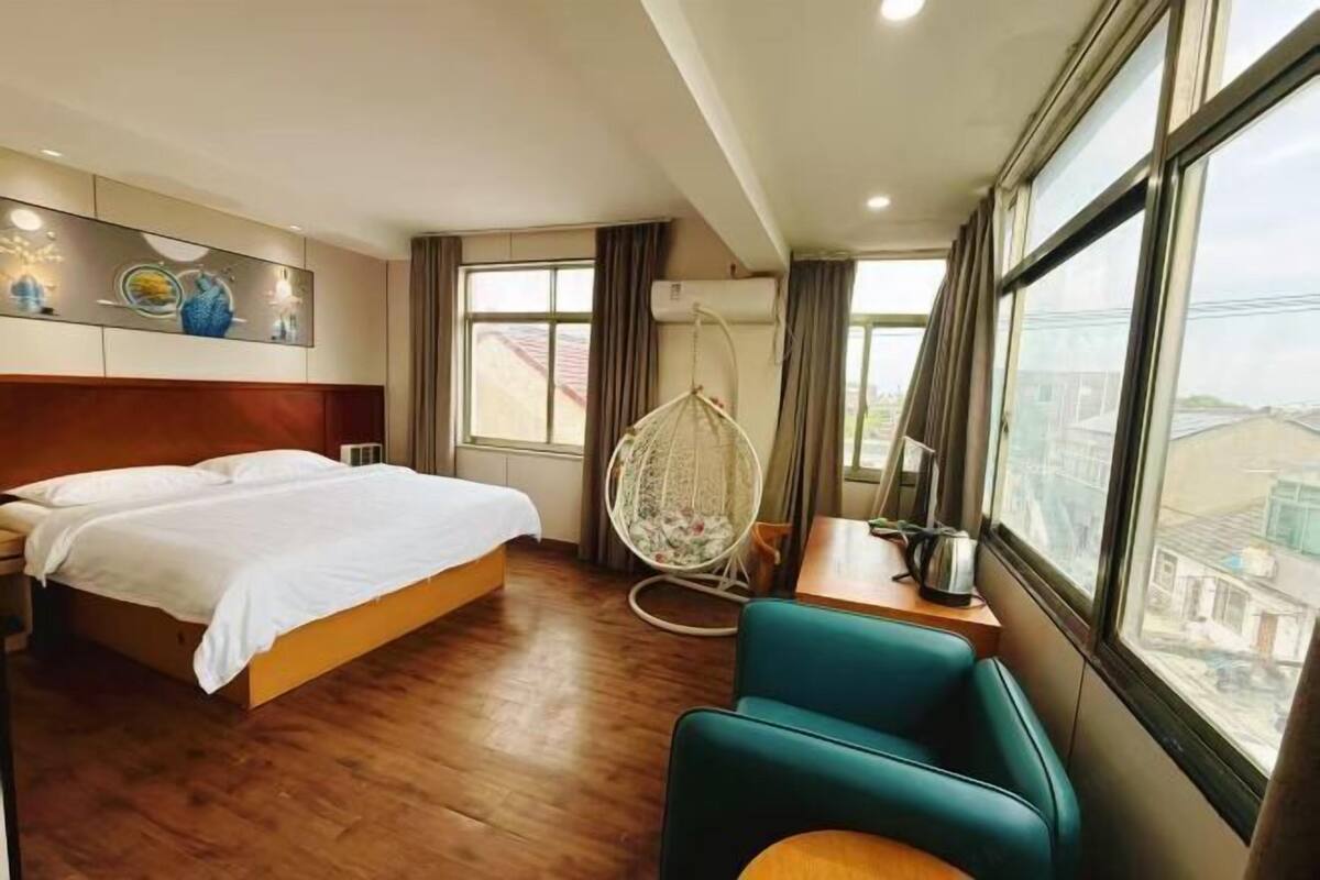 A hotel room with a bed, a chair, a desk, and a large window offering a city view.