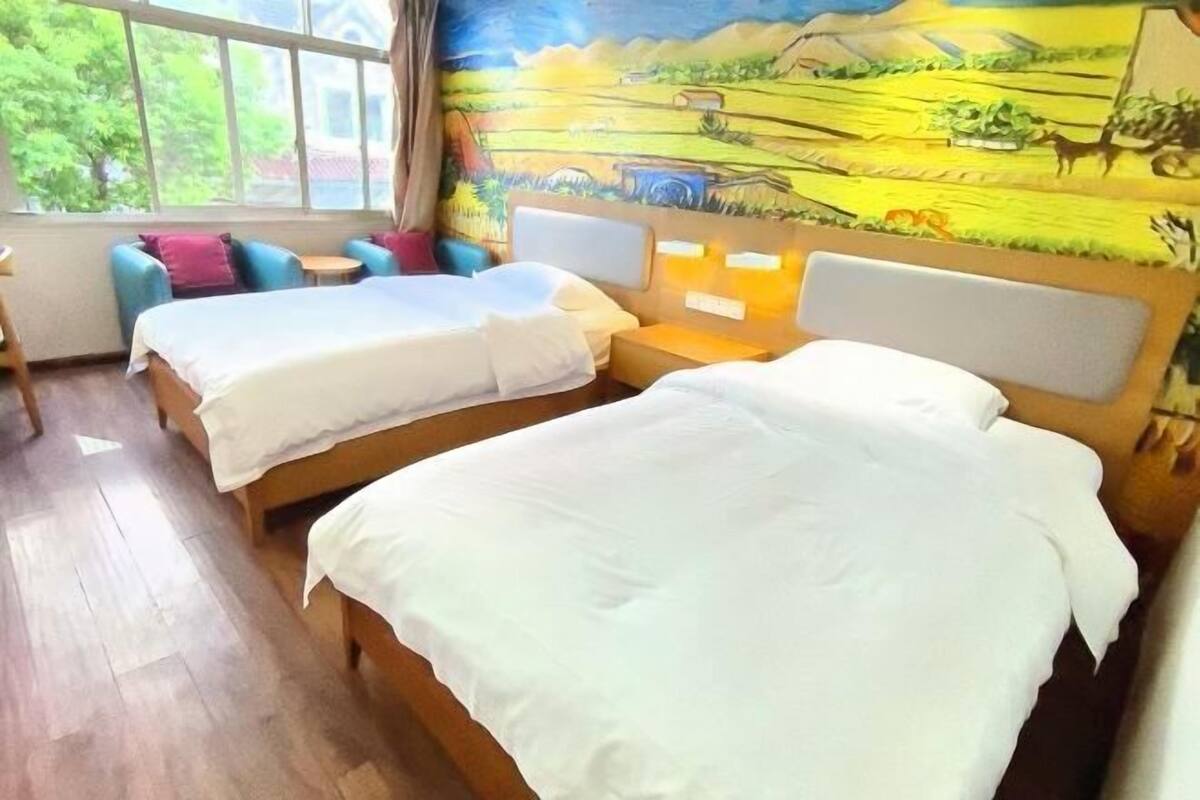A hotel room with two beds, a mural on the wall, and a view of greenery outside.