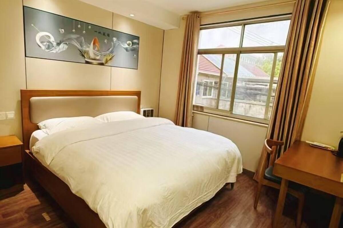 A hotel room with a bed, a desk, a chair, a window, and a painting on the wall.