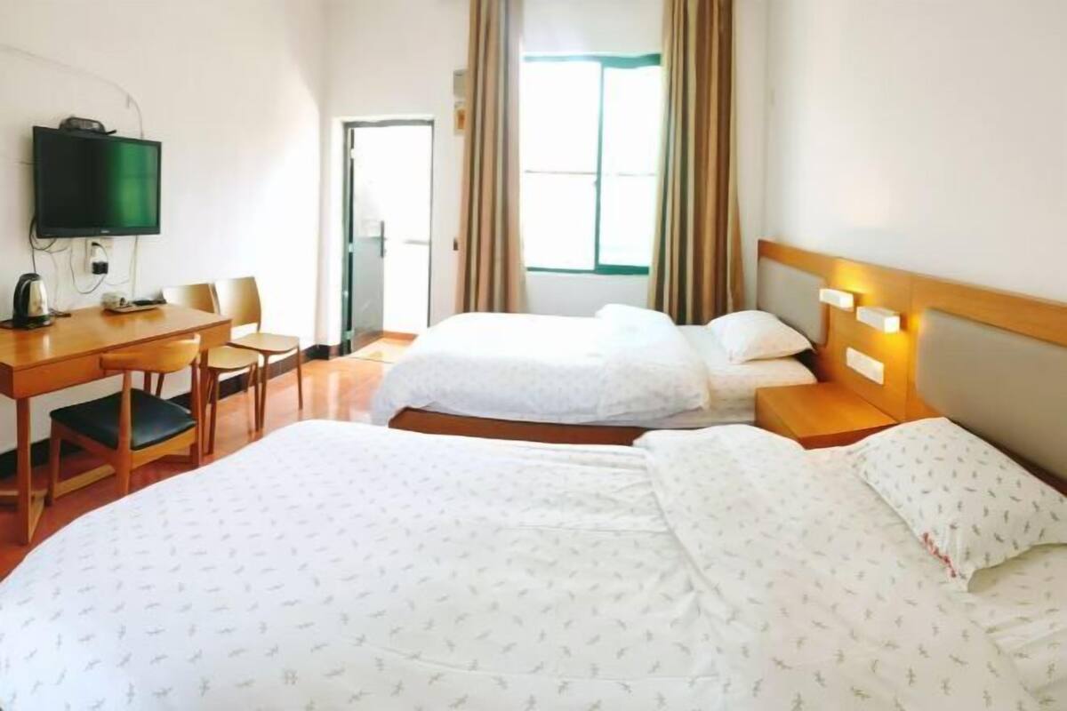 A hotel room with two beds, a desk with a chair, a television, and a window with curtains.