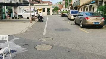 A street view with parked cars and a motorcycle, buildings on either side, and a manhole cover in the center of the road.