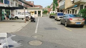 Eine Straße mit parkenden Autos und einem Motorrad, Gebäude mit Geschäften sowie ein Straßenabdeckung.