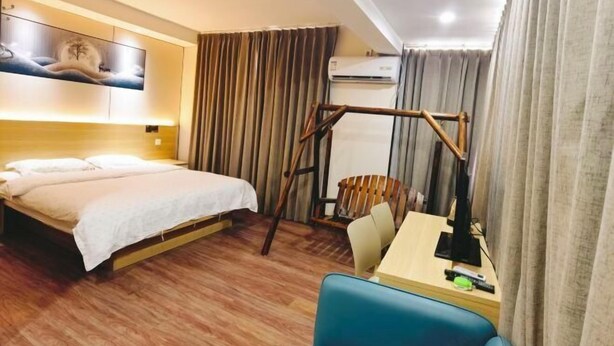 Ein Hotelzimmer mit Bett, Schreibtisch, Stuhl, Vorhängen, einer Klimaanlage und einem an der Wand befestigten Kunstwerk.