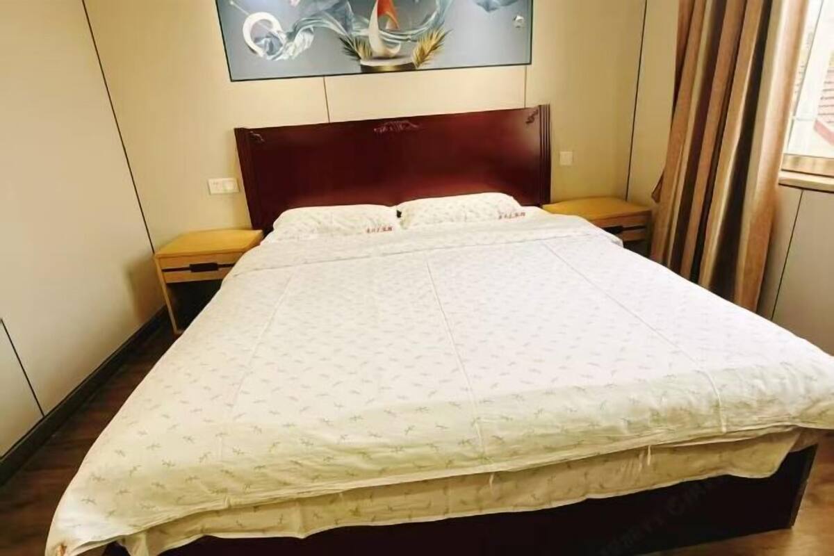 A hotel room with a large bed, a wooden headboard, a nightstand, and a wall-mounted artwork.