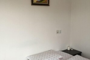 Une petite pièce simple, avec un lit simple, une table de chevet et une prise électrique au mur.