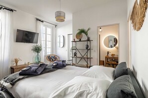 Un dormitorio moderno con una cama grande, un televisor en la pared, una estantería con plantas y un espejo con luz redonda.