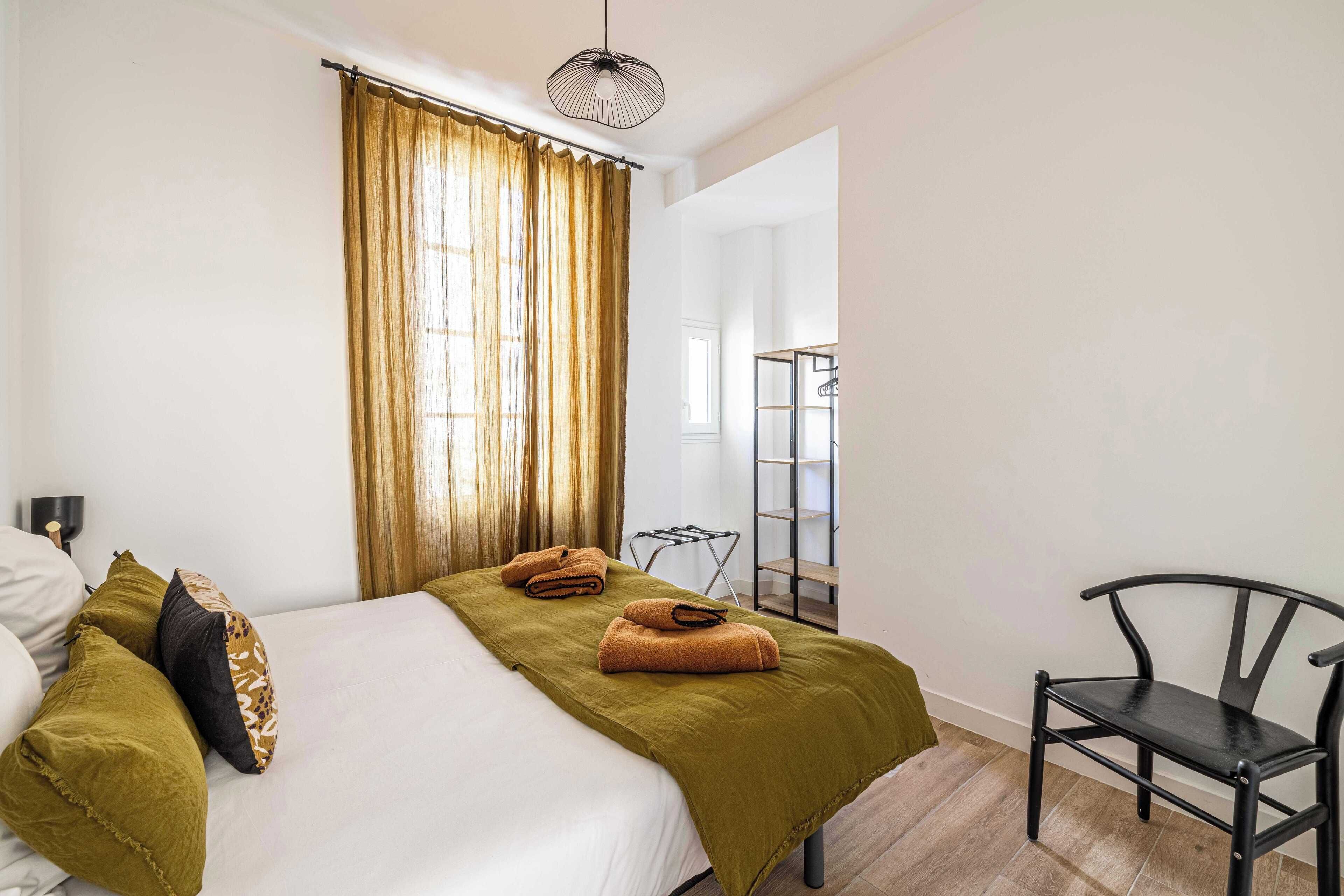 Une chambre d’hôtel avec un lit, une chaise et une étagère.