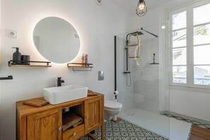 Ein modernes Badezimmer mit großem Spiegel, Waschtisch aus Holz, weißem Waschbecken, Toilette und einer Duschkabine aus Glas.