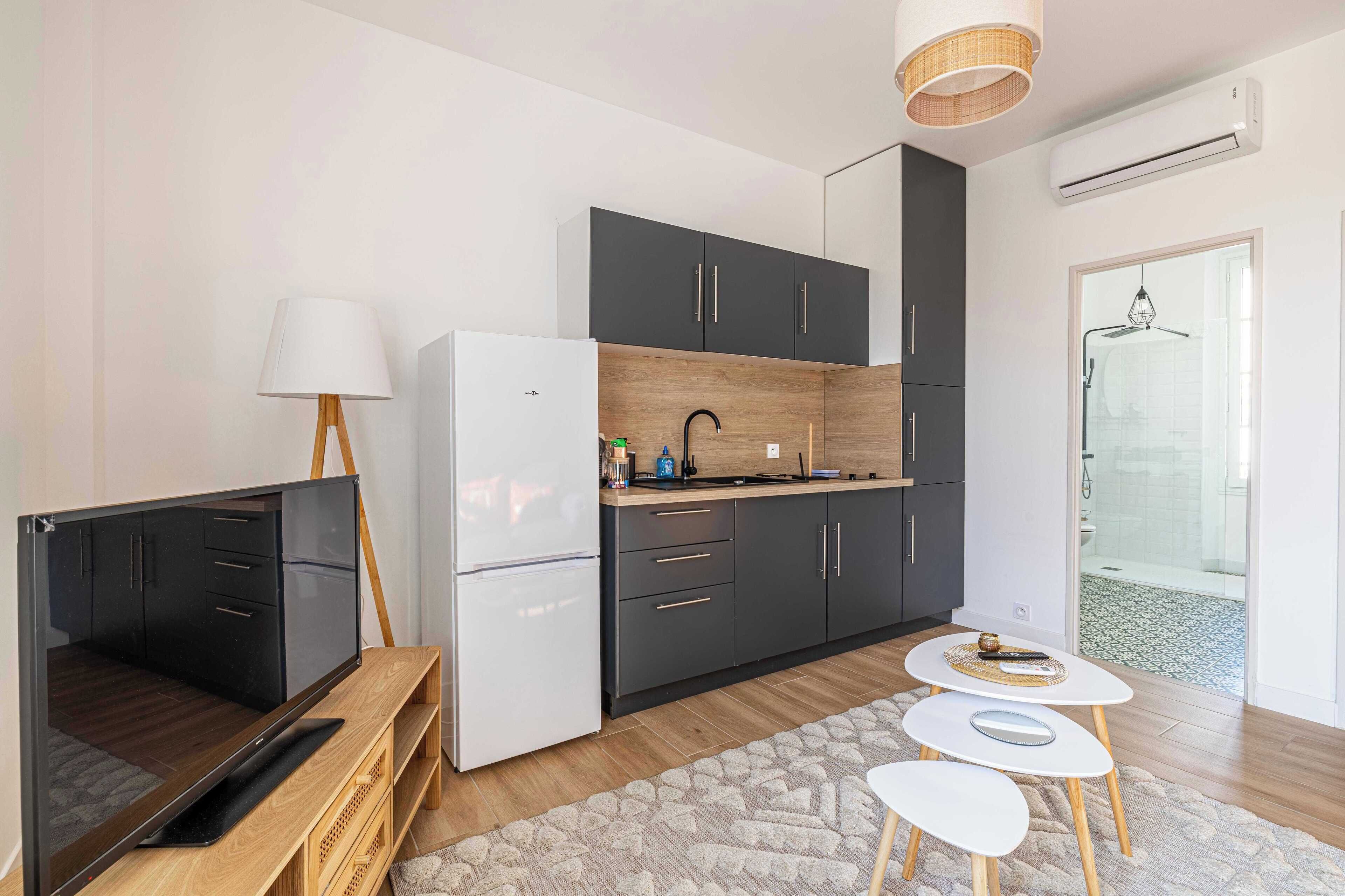 A modern kitchen with dark cabinets, a white refrigerator, and a small dining area with two stools.