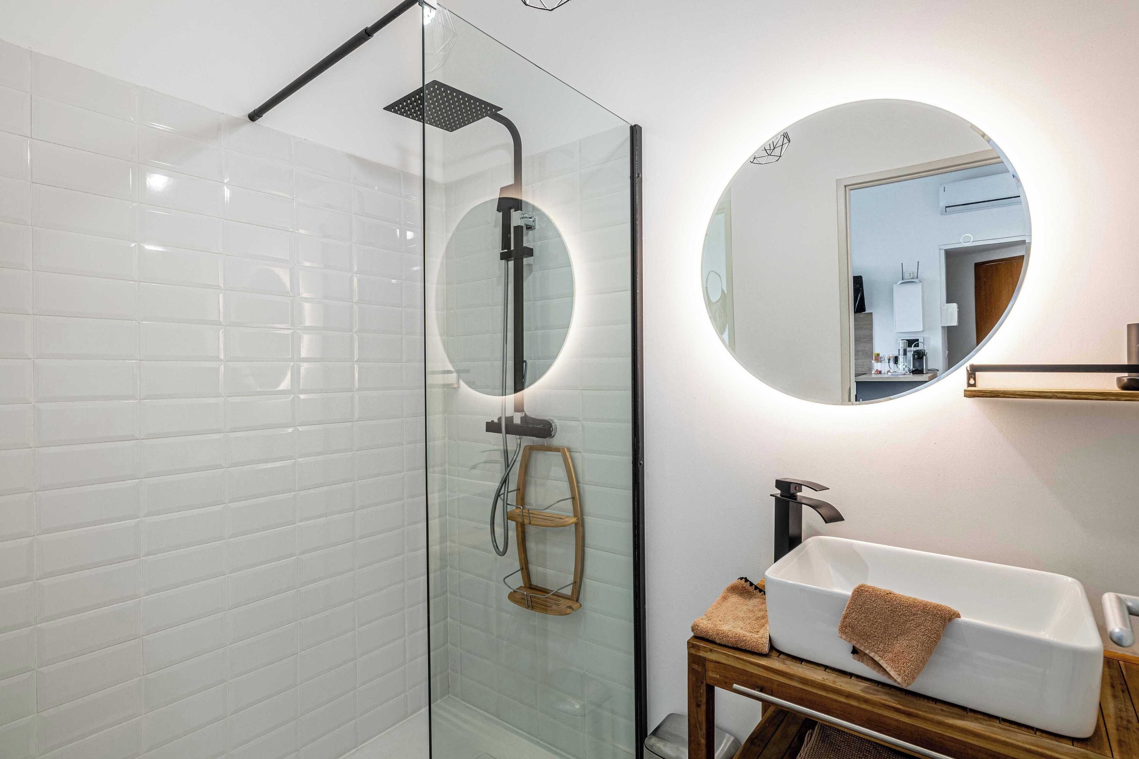 Une salle de bain moderne avec une douche à parois de verre, un lavabo blanc avec une serviette et un miroir rond.