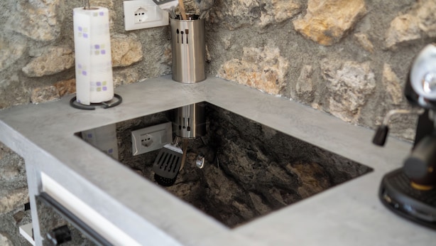 Une cuisine avec un mur en pierre, un évier et un appareil en acier inoxydable.