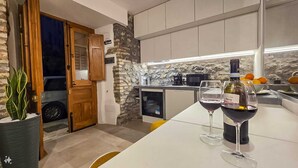 Une cuisine moderne avec un mur d’accent en pierre, des armoires en bois et un coin repas agrémenté de deux verres à vin.