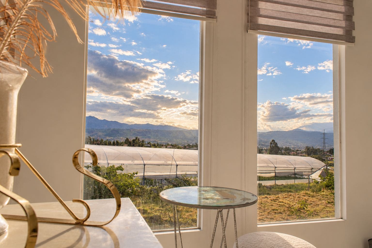 A room with a large window overlooking a landscape with mountains and a greenhouse.