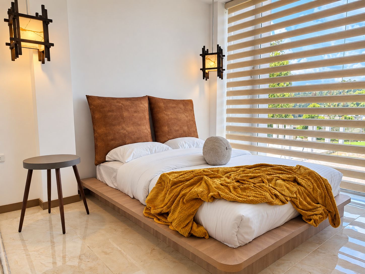 A bedroom with a bed, a round stool, and two wall-mounted light fixtures.