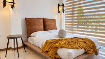 A bedroom with a bed, a round stool, and two wall-mounted light fixtures.