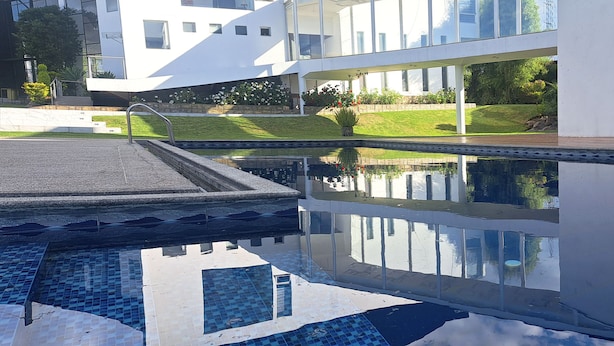 A modern building with a swimming pool, reflecting the building's facade and surrounding greenery. - HOTEL QUINTA KRYSTAL BOUTIQUE (Sangolqui)
