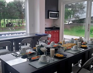 A dining area with a long table set for breakfast, a microwave above it, and a view of the outdoors. - HOTEL QUINTA KRYSTAL BOUTIQUE (Sangolqui)