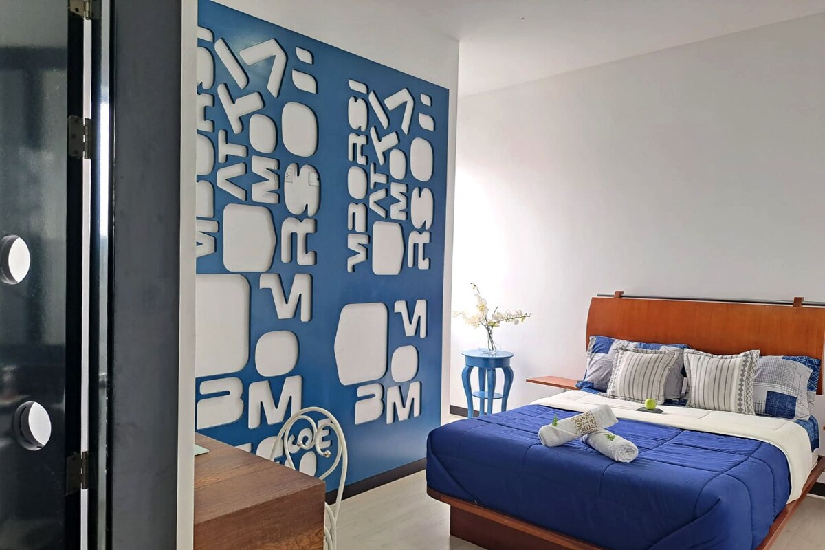 A modern bedroom with a blue bedspread, wooden headboard, and a decorative wall with cut-out letters.