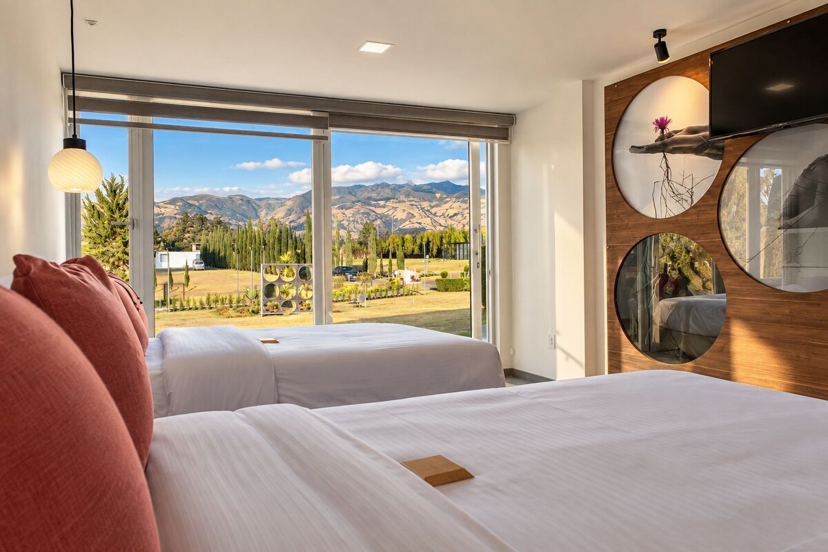 A hotel room with two beds, large windows, and a view of mountains.