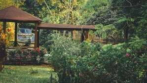 A gazebo with a wooden roof and a metal railing, surrounded by lush greenery and flowering plants. - Bungalow with Swimming Pool in Nature (Palin)