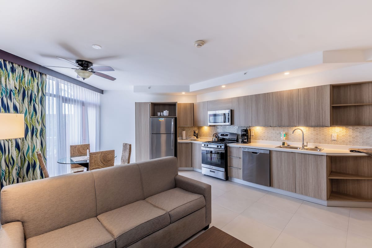 A modern kitchen with a built-in microwave, oven, and dishwasher, and a living area with a sofa and dining table.