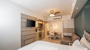 A modern hotel room with a large bed, a dining area, a kitchenette, and a ceiling fan. - Paradise Beach Villas (Oranjestad)