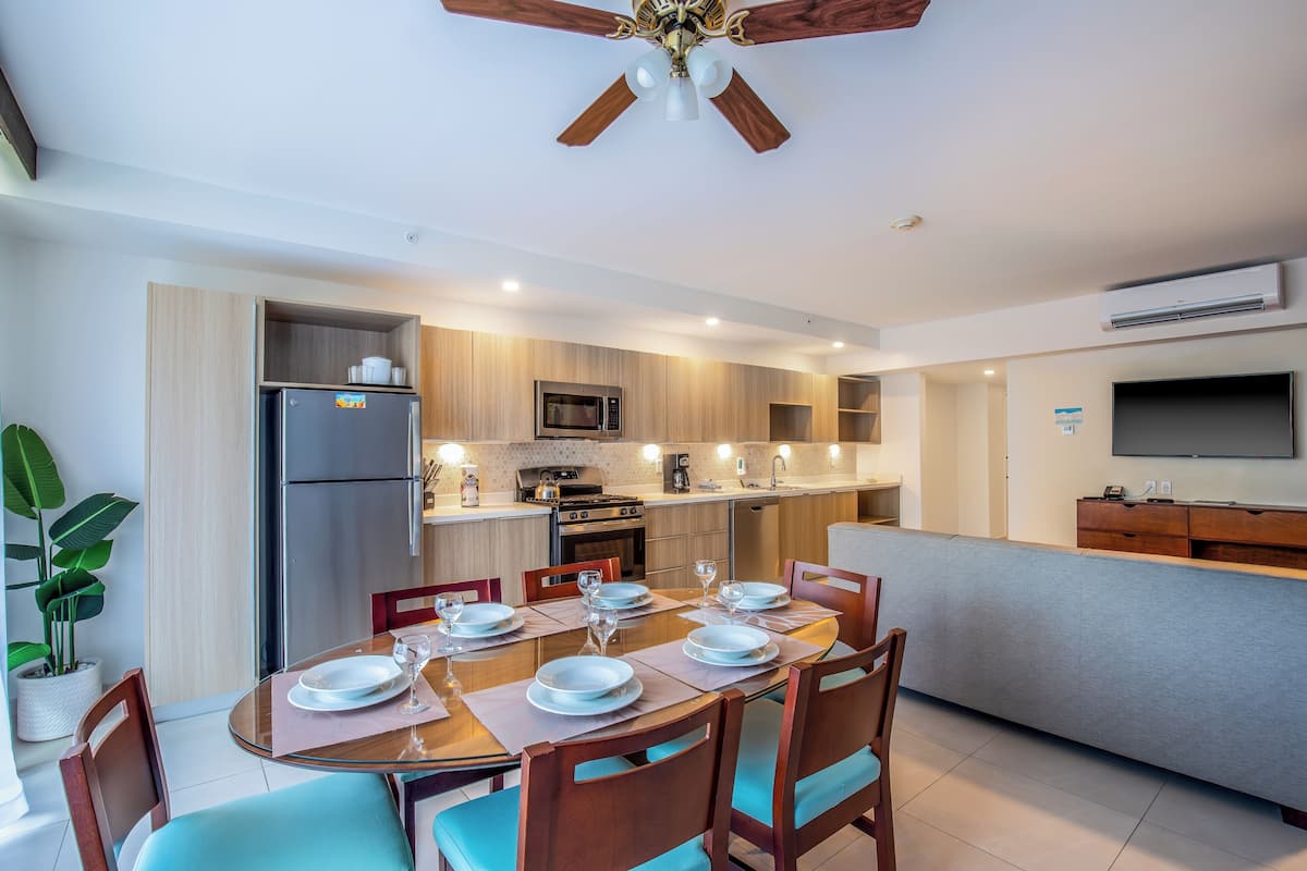 A modern kitchen with a built-in oven, microwave, and refrigerator. There is a dining table set with plates and glasses.