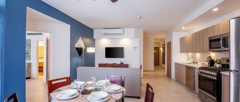 Une cuisine moderne avec un coin repas, comprenant une table à plateau en verre, des chaises en bois, un ventilateur de plafond et des appareils électroménagers intégrés.