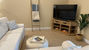 A living room with a beige sofa, a coffee table with a book, a wooden TV stand, and a potted plant. - Beautiful Saltwater Front Home with a Private Pool! (Cape Coral)