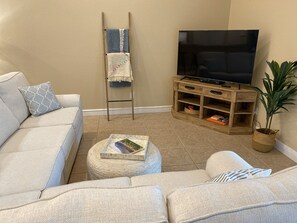 Ein Wohnzimmer mit einem beigefarbenen Sofa, einem Couchtisch mit einem Buch, einer Holz-TV-Bank und einem Blumentopf.