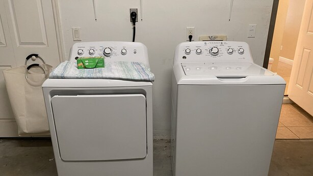 Two front-loading washing machines in a laundry room with a white door and tiled floor. - Beautiful Saltwater Front Home with a Private Pool! (Cape Coral)