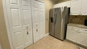 A kitchen with white cabinets, a stainless steel refrigerator, and beige tiled flooring. - Beautiful Saltwater Front Home with a Private Pool! (Cape Coral)