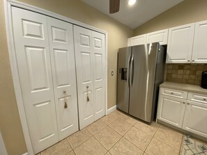 Eine Küche mit weißen Schränken, einem Edelstahlkühlschrank und beige gefliestem Boden.