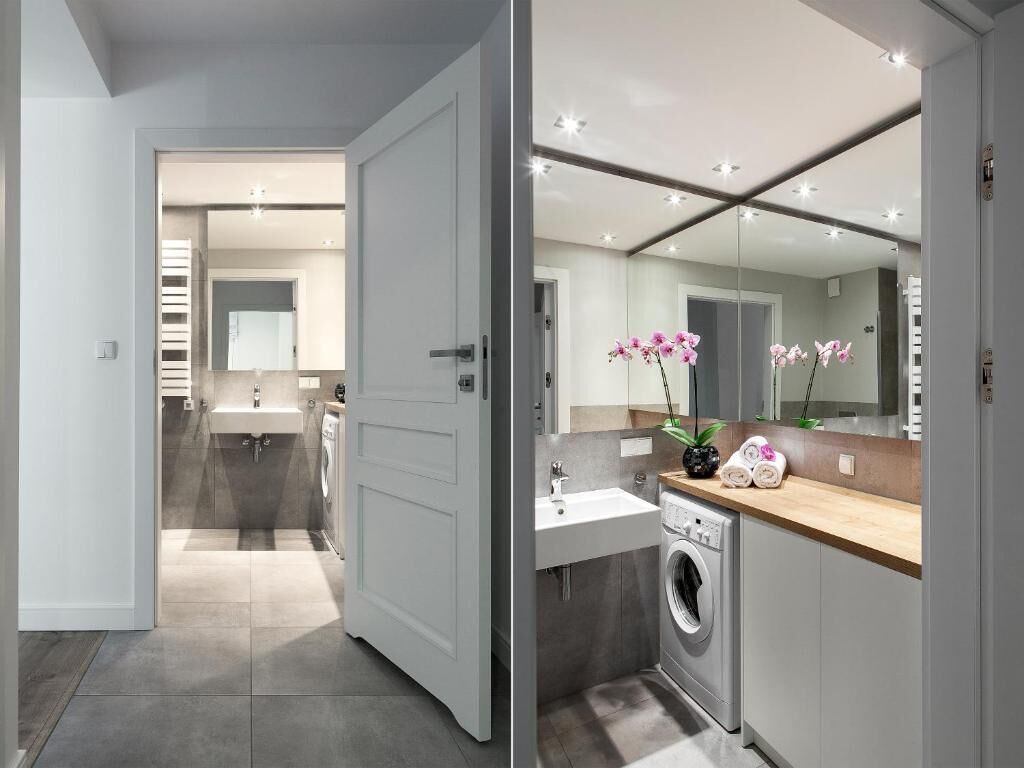 A modern bathroom with a large mirror, a sink, a washing machine, and a toilet.