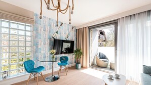 Un salon moderne avec une table en verre, deux fauteuils bleus, un canapé blanc et une grande fenêtre donnant sur l’extérieur.