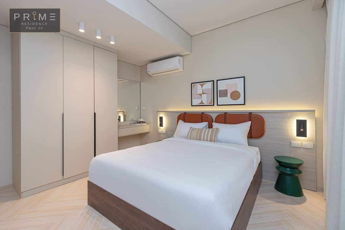 A modern bedroom with a large bed, a wardrobe, a vanity, and a green side table.